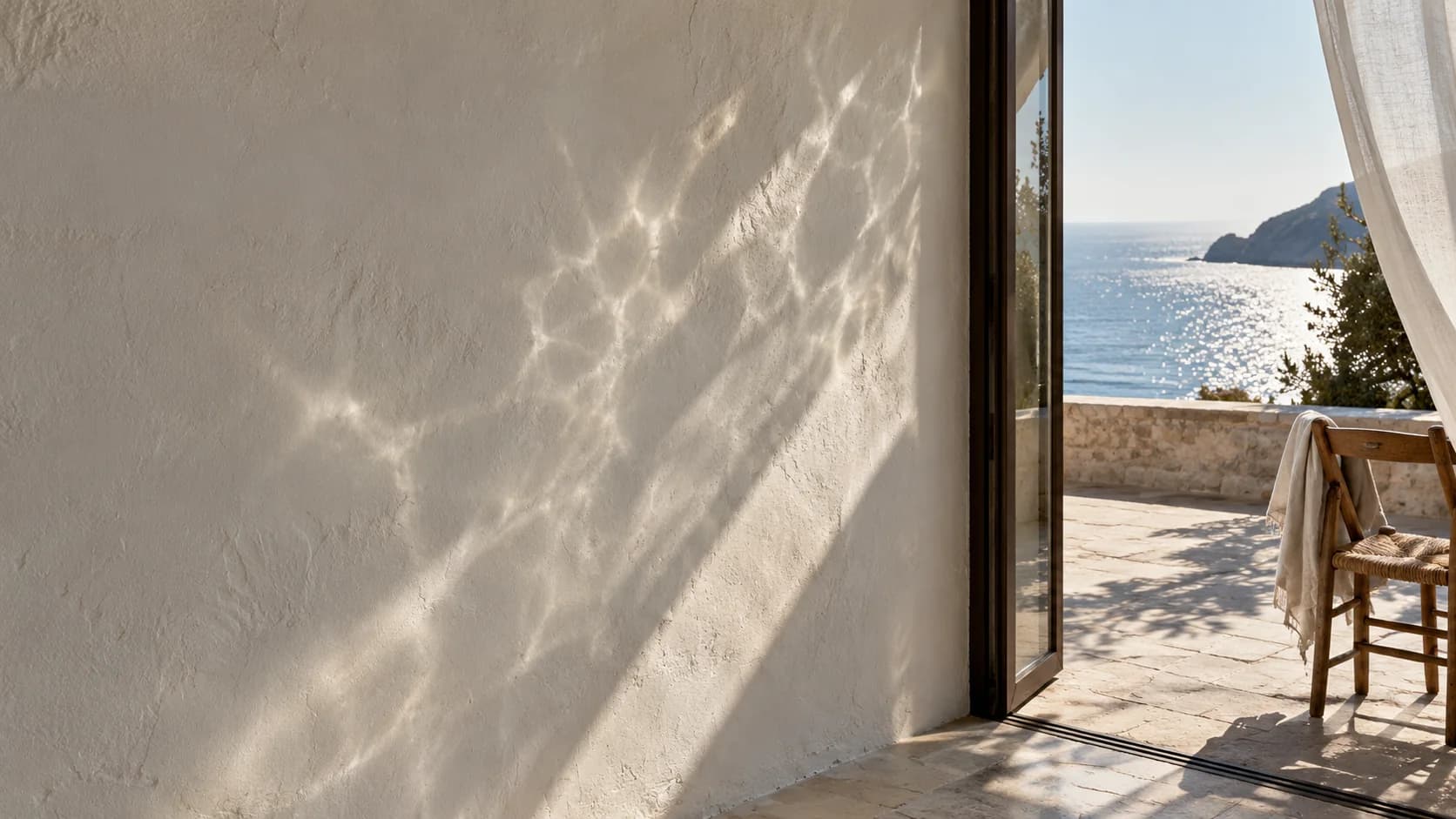 An ivory coastal gallery wall in daylight, with a linen curtain lifting beside an open window and a quiet chair.