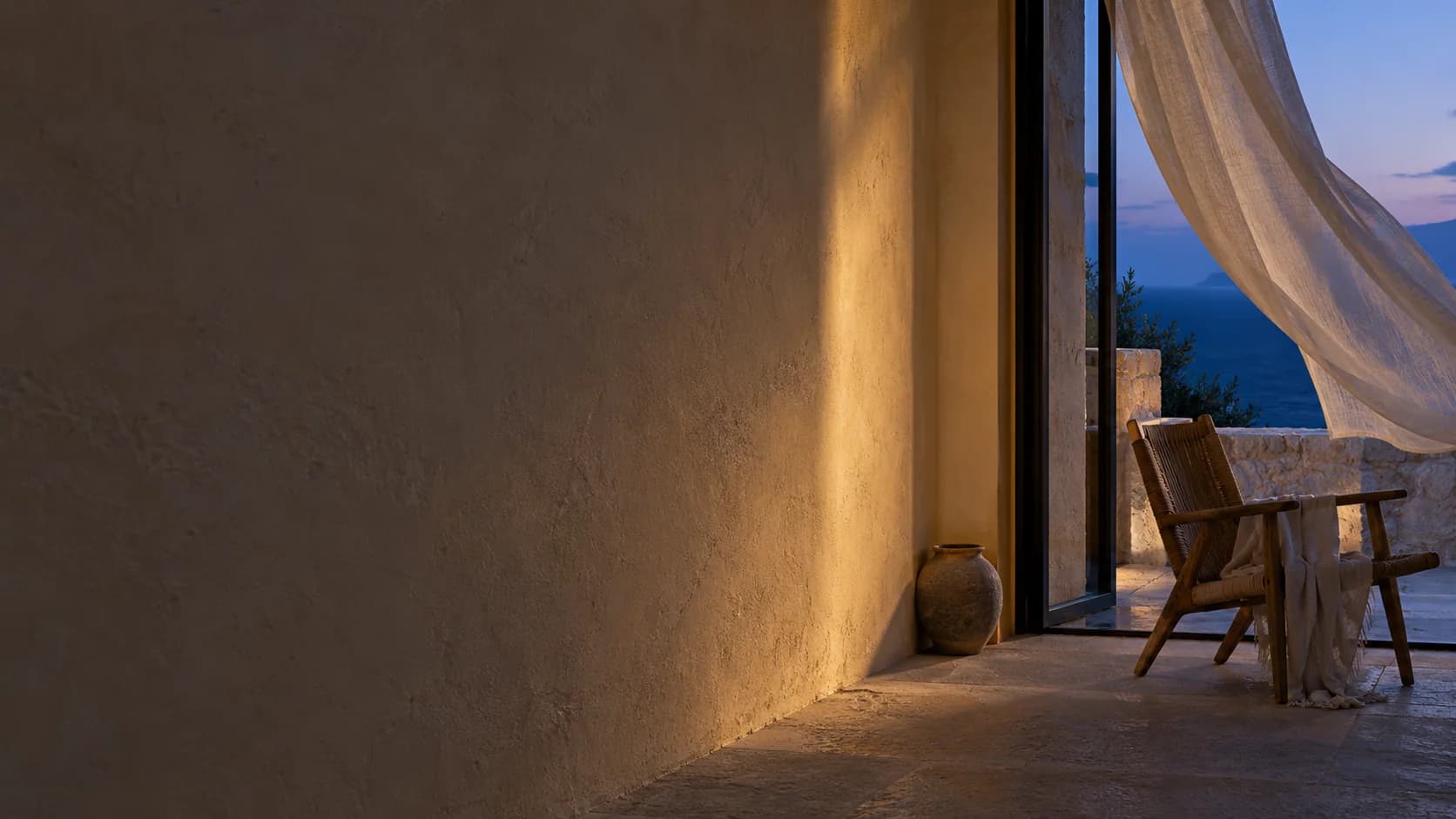 A coastal gallery at blue hour, a narrow ivory reflection on the wall and a linen curtain lifting beside an open window.