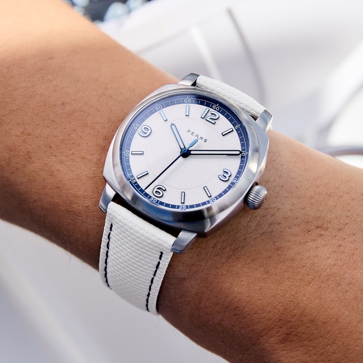 A silver wristwatch with a white dial and white strap worn on a person’s wrist.